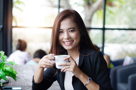 亚洲女商人在咖啡厅喝时微笑并端着咖啡杯喝早晨女桌子图片