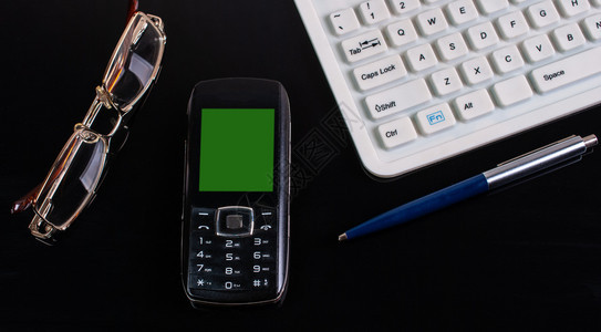 白色的工作商业附件键盘眼镜圆球笔和电话带有绿色屏幕办公室服务台并配有键盘电话笔和眼镜沟通图片