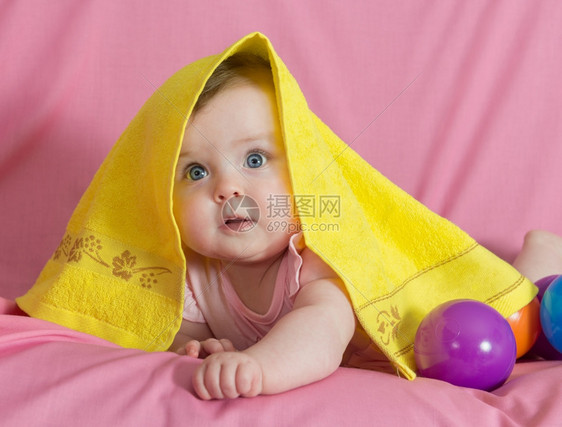 清白的新人类美丽快乐女婴带着粉红背景的黄色毛巾图片