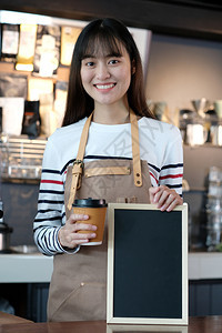 菜单在咖啡馆的柜台背景食物和饮料概念上年轻女青咖啡师拿着面笑脸的白黑纸板员工自助餐厅图片
