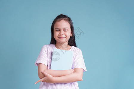 常设学习亚洲快乐的小女孩站着拿书关于蓝色背景的书孤立愉快图片