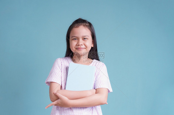 常设学习亚洲快乐的小女孩站着拿书关于蓝色背景的书孤立愉快图片