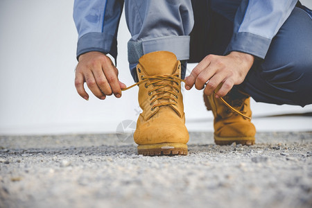 合身鞋带穿男人跪在地上为工人打领带鞋业靴子近距离拍到人手绑鞋的镜头为他建造筑用的棕色靴子紧贴男人把鞋子绑起来用做概念图片