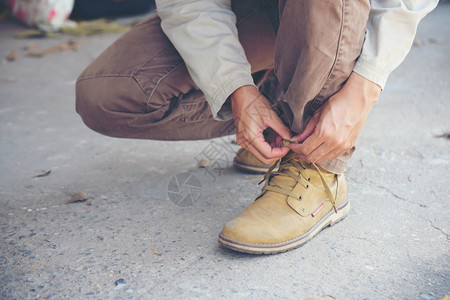 户外健康男人跪在地上为工人打领带鞋业靴子近距离拍到人手绑鞋的镜头为他建造筑用的棕色靴子紧贴男人把鞋子绑起来用做概念年轻的图片