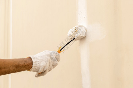 穿着白布手套用滚筒在混凝土墙上涂白色的衣物一种男人行业图片
