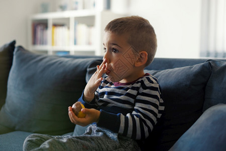 老的坐在沙发床上小孩手拿着巧克力糖吃一边看着电视在嘴舔手指头TVtvlickingfingerinmouthsideview男生图片