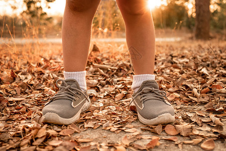 穿着运动鞋站在人行道上路面的年轻女孩与夏季公园干叶站在一起的青年女孩近身健康生活方式概念腿户外锻炼图片