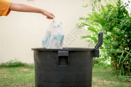 人类绿色保护手把垃圾扔进塑料袋花园的垃圾桶图片