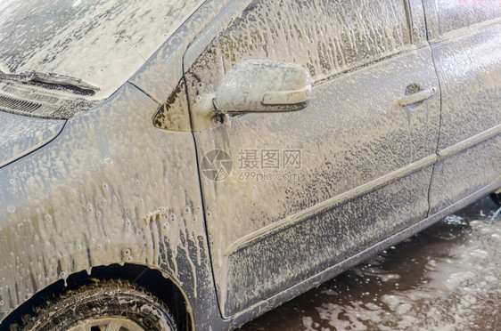 肮脏的蓝色车在洗店用泡沫洗车喷湿的图片