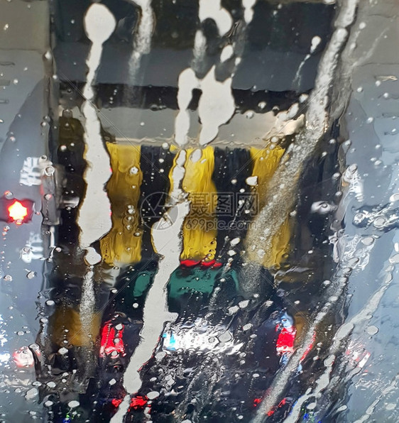一辆汽车在洗一个通过湿风挡玻璃的视图刷子在洗车时技术自动化的图片