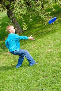 快乐的小男孩在青草上玩飞盘蓝色的牛仔裤图片