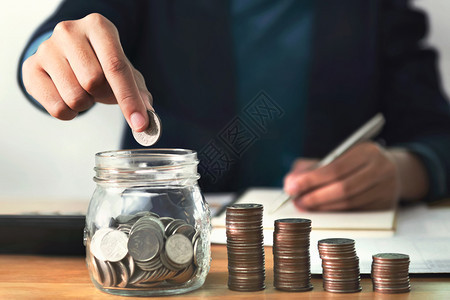 利润关心商人业妇女将硬币放在玻璃杯中节约金钱和财务会计的概念上图片