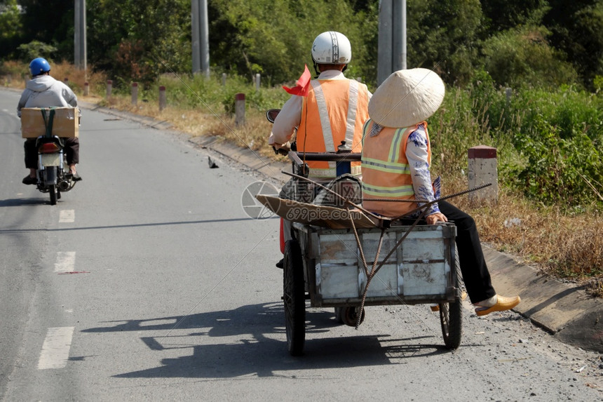 两位清洁卫生工作者一起在乡村公路上行走男子骑摩托车与拖箱转接妇女两人在下班后路上相伴他们的影子反射到路面越南帽子女亚洲人图片