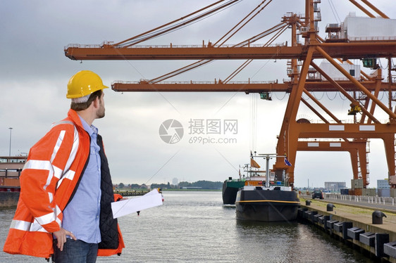 反光的手一个穿着安全大衣和硬帽检查集装箱港口大型起重机的人商业的图片