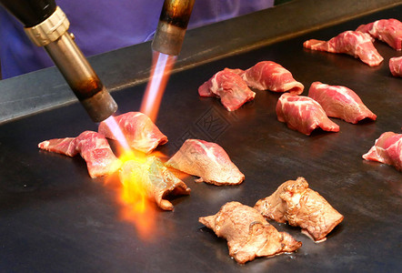 男人热厨师用喷灯烧一小片华玉牛肉做寿司焦糖热的图片