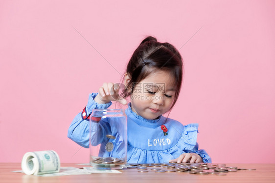 金融女儿这小孩把硬币放在一个透明的玻璃罐里钱储蓄的概念注图片
