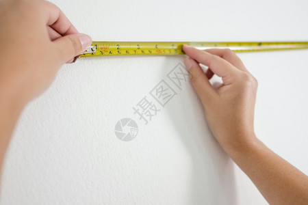 成人在室内积极的白色墙上测量黄磁带女用手图片
