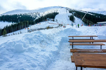 全景山斯洛伐克冬季滑雪度假胜地Jasnaovercrowd空木板椅和滑雪坡边的斜休息点附近的桌景观图片