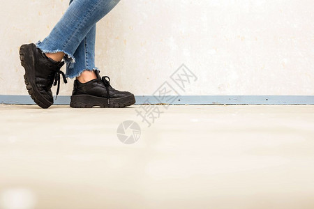 脚丫子穿着蓝色牛仔裤和运动鞋的女士穿着蓝色牛仔裤和运动鞋走在白墙附近时尚概念特写镜头穿着白色真皮运动鞋的女士穿着蓝色牛仔裤和运动图片
