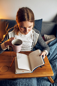 新闻业日记思维做笔阅读和学习的年轻妇女在隔离期间坐家中床上写作时从笔记本女孩写作杂志中读到图片