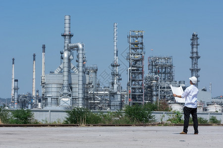 白色的难贮存工程师身着白头盔站在炼油厂背景上站立的炼油厂工程师图片
