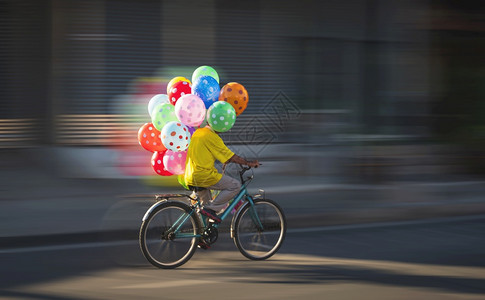 城市的成熟黄昏时在街上骑自行车的亚洲气球销售商运动模糊骑术图片