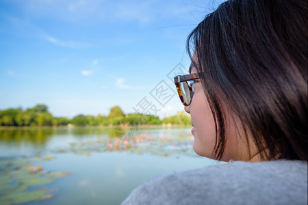 池塘看着沼泽附近的自然景观和莲花快乐地看着她的面部戴着眼镜坐在轻松的休息中公园头发图片