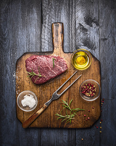 吃超额木板生来新鲜的大理石牛肉排配有叉和在蓝木本底的锈制切削板上调味料图片