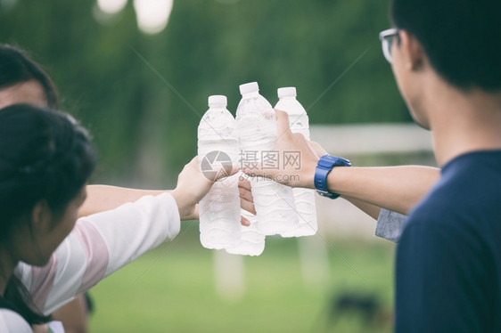 在校园草坪上拿着水瓶碰杯的学生群体图片