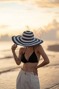 穿着顶比基尼和白色长裤戴帽子的妇女支撑美丽海滩图片