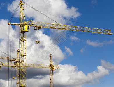生长摩天大楼在城市新区建筑工地上造高黄色架起重机Arrows站在蓝色天空的顶层建筑起重机对面颜色图片