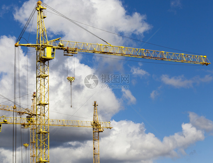 生长摩天大楼在城市新区建筑工地上造高黄色架起重机Arrows站在蓝色天空的顶层建筑起重机对面颜色图片