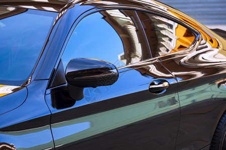 玻璃铬合金关注汽车机翼镜面在现代黑色汽车表面建筑和蓝天空的模糊多彩反射式下聚焦于车翼镜面细节图片