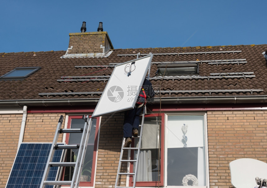绿色太阳的男人用能电池板攀登屋顶的梯子图片