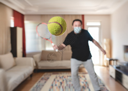 在Covid19Corona疫情检中在家里打网球时戴保护医疗面具的男子在家中打网球运动电晕男人图片