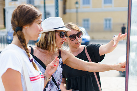 帮助友谊夏天3名女旅游客在假期的暑日观看科孚镇旅游目的地信息板上图点在度假时观看Corfu镇旅游目的地信息板上图位置图片