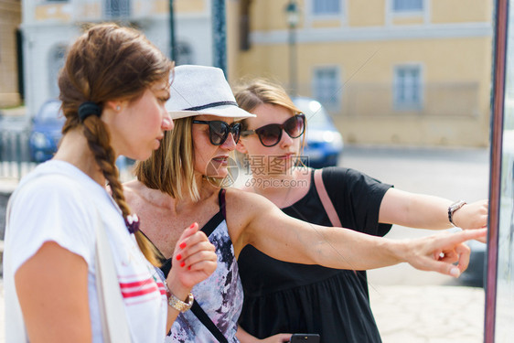 参观女孩3名旅游客在假期的暑日观看科孚镇旅游目的地信息板上图点在度假时观看Corfu镇旅游目的地信息板上图位置咨询图片