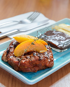 蓝色盘子和木桌上的餐具装有桃子和薯条的加格列猪排牛片刀具肉叉图片
