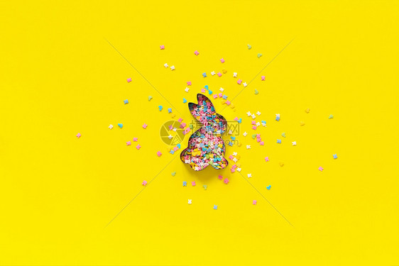复活节兔子形状和散布在黄纸上的五彩糖果浇头概念复活节日背景制空间顶视图复活节兔子形状和散射在黄纸上的五彩糖果浇头概念复活节日背景图片