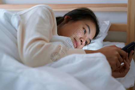 美丽的家互联网亚洲女人晚上躺在卧室里时使用智能手机的亚洲女人图片