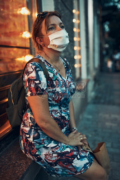 穿关心晚上在市中购物后坐在咖啡店前门户外口的年轻女子戴面罩以避免感染和防止疾病在冠状腺毒传播时蔓延她们戴着面罩避免感染防止疾的传图片