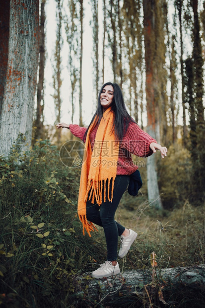 女士秋天走道妇白穿着黄色围巾和红羊毛球衣在树干上走过森林白天穿戴黄色围巾和红羊毛运动衫图片