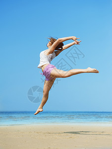 旅行玩海洋美丽的精力充沛年轻女子在海滩上跳跃图片