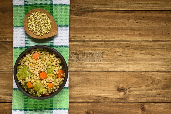 蔬菜食物卷心由小麦谷物香菜卷胡萝卜南瓜和红洋葱制成的Vegan炖肉上面小盘子的麦粒用自然光照在黑木头上图片