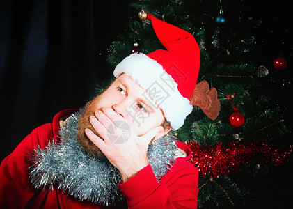 情感颜色真实的穿着圣诞老人红色西装的面部胡子人向着圣诞树黑暗背景看去选择焦点在圣诞老人红衣服中的粉丝胡子人选择关注点图片