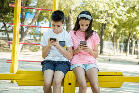 儿童在公园的黄色儿童结构中看手机他们坐在一个黄色儿童建筑里年轻的坐着沟通图片