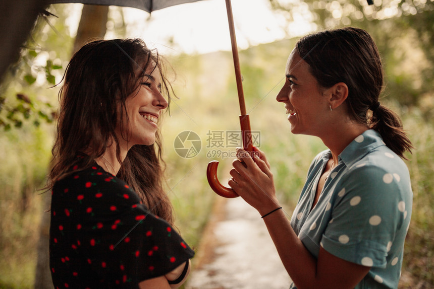 白天约会浪漫两名年轻妇女在田地上拿着雨伞站在身裙子和运动鞋的树丛中站立图片