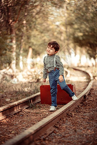 穿着旧衣服的可爱小男孩站在废弃铁路上手里拿着旧式提箱的行李孩子们相机可爱的图片