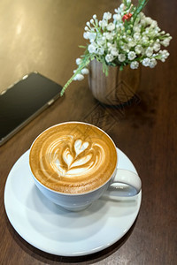 电话咖啡因桌上的杯在店装饰假花和手机上装着假花朵桌面观景饮料概念曼谷图片