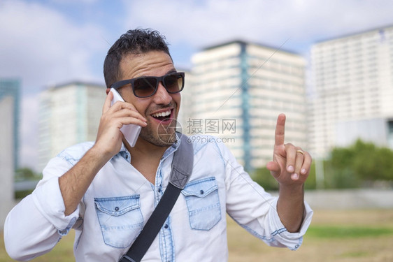 青年男子在街上使用手机而在户外微笑成人太阳镜打电话图片